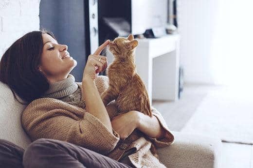 Mujer sentada en una butaca sosteniendo un gato atigrado anaranjado y tocándole suavemente la nariz