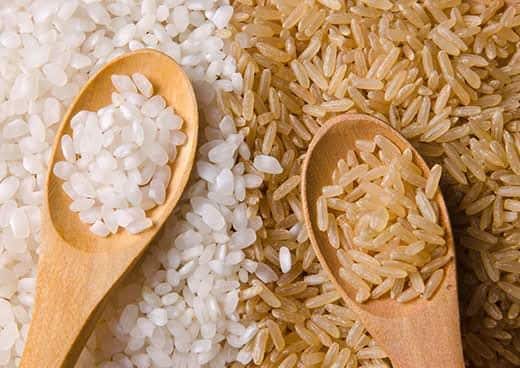 Montones de arroz blanco e integral, cucharas de madera cargadas de arroz.